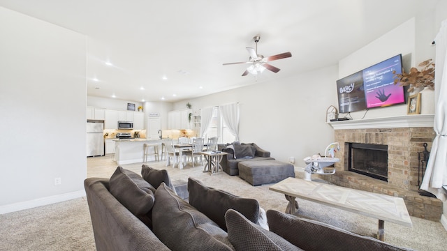 living room with a brick fireplace, ceiling fan, baseboards, recessed lighting, and light carpet