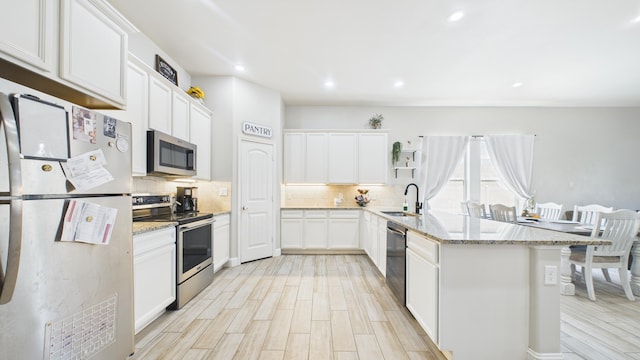kitchen with light wood-style flooring, backsplash, a peninsula, and appliances with stainless steel finishes