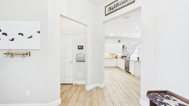 hallway with baseboards, light wood-style flooring, and a sink