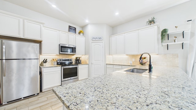 kitchen featuring light stone countertops, stainless steel appliances, open shelves, a sink, and white cabinetry
