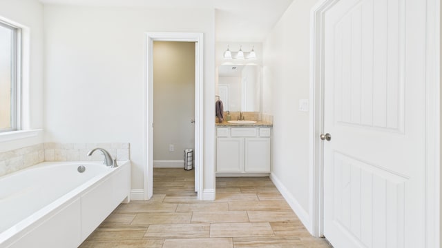 bathroom with wood finished floors, a garden tub, vanity, and baseboards