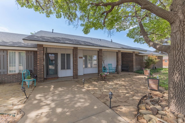 back of property featuring a patio, brick siding, and a shingled roof