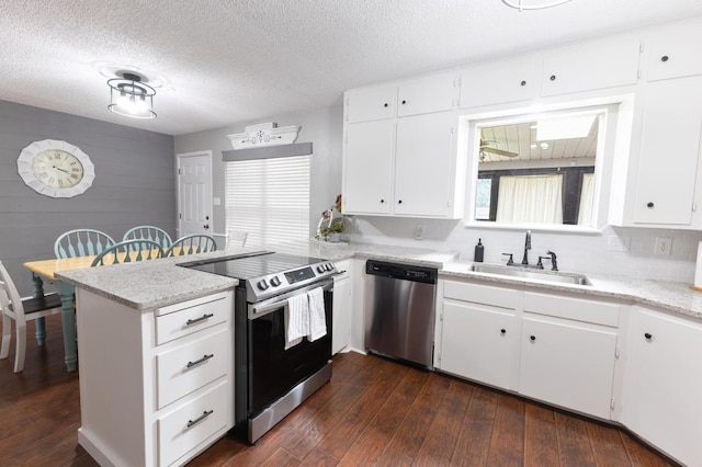 kitchen with appliances with stainless steel finishes, white cabinetry, sink, dark hardwood / wood-style flooring, and kitchen peninsula