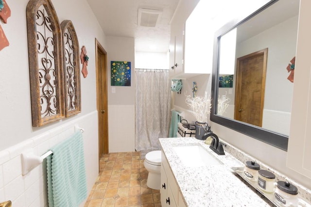 bathroom featuring a wainscoted wall, toilet, curtained shower, vanity, and visible vents