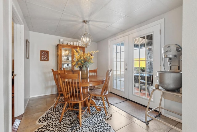 tiled dining space with a drop ceiling, a notable chandelier, and french doors