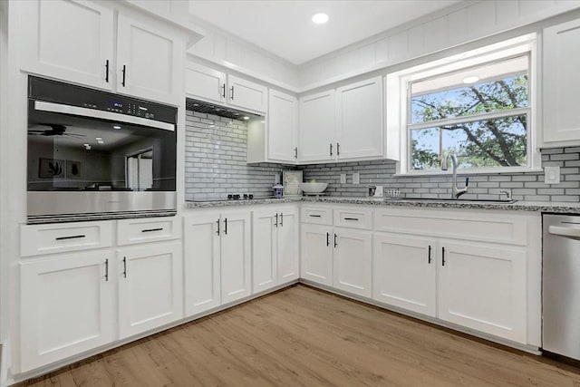 kitchen with light wood finished floors, a sink, backsplash, white cabinetry, and stainless steel dishwasher