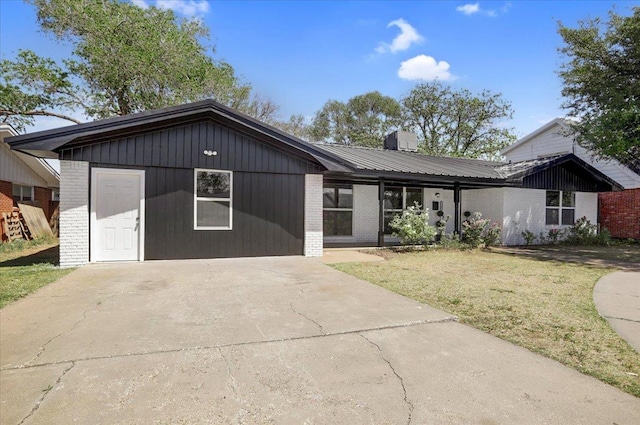 view of front of property featuring a front yard, concrete driveway, brick siding, and metal roof