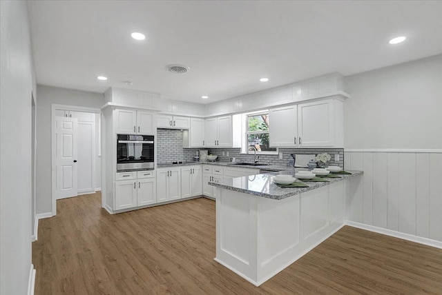 kitchen with sink, light hardwood / wood-style flooring, white cabinetry, light stone counters, and oven