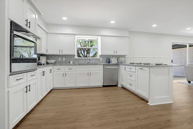 kitchen with a peninsula, white cabinets, appliances with stainless steel finishes, and a sink