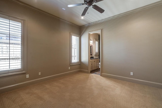 spare room featuring carpet, a healthy amount of sunlight, crown molding, baseboards, and ceiling fan