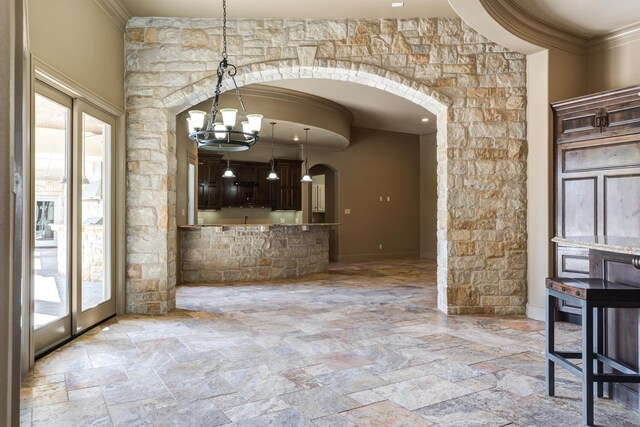 unfurnished dining area with arched walkways, stone tile floors, crown molding, and an inviting chandelier