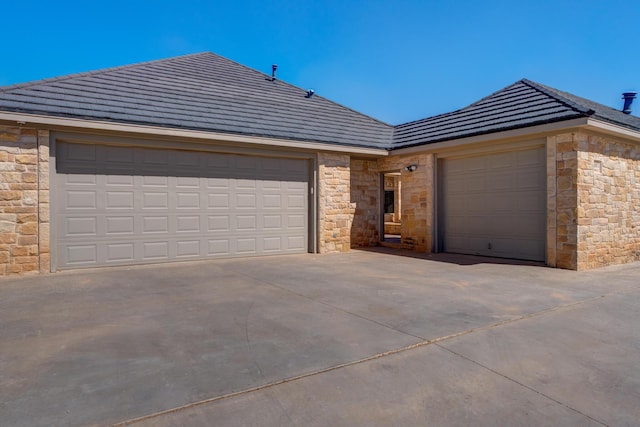 ranch-style home with a garage, driveway, stone siding, and a tile roof
