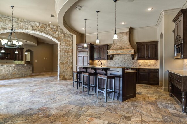 kitchen with arched walkways, stainless steel microwave, tasteful backsplash, stone tile floors, and custom exhaust hood