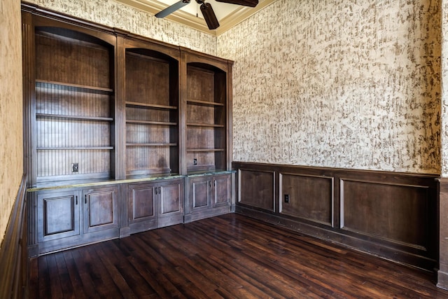 empty room with ceiling fan, dark wood-style flooring, ornamental molding, and a wainscoted wall