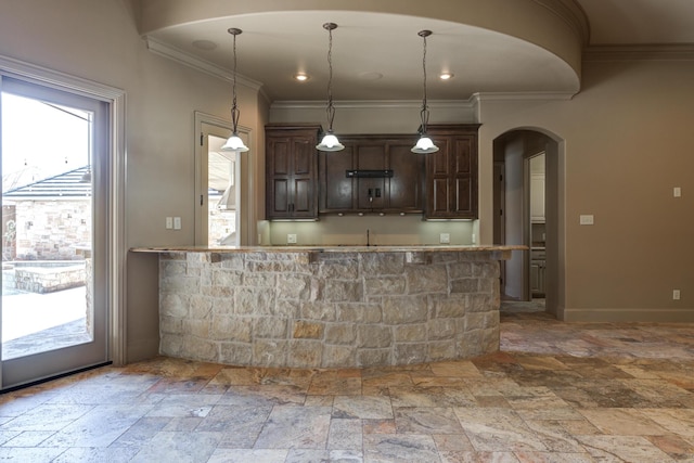 kitchen featuring ornamental molding, arched walkways, stone tile floors, and dark brown cabinetry