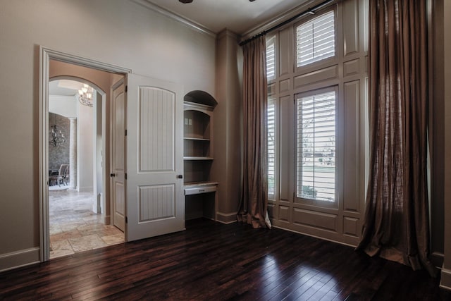 unfurnished room with a towering ceiling, arched walkways, crown molding, baseboards, and hardwood / wood-style flooring