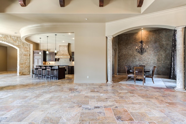 dining space featuring stone tile flooring, arched walkways, a notable chandelier, ornate columns, and ornamental molding