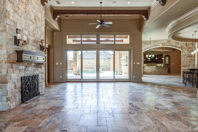 unfurnished living room featuring ceiling fan with notable chandelier, stone tile flooring, arched walkways, and ornamental molding