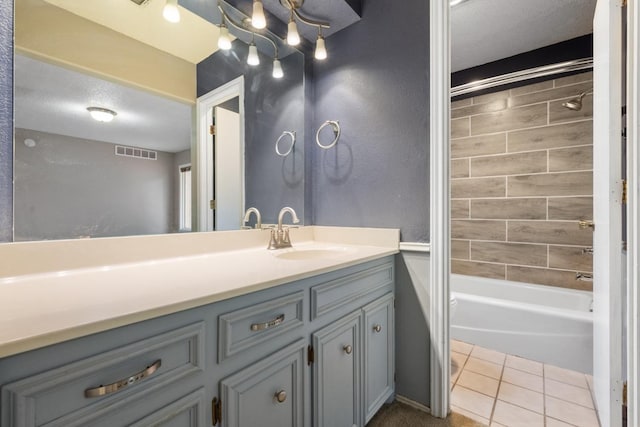 bathroom with tile patterned flooring, vanity, a textured ceiling, and tiled shower / bath