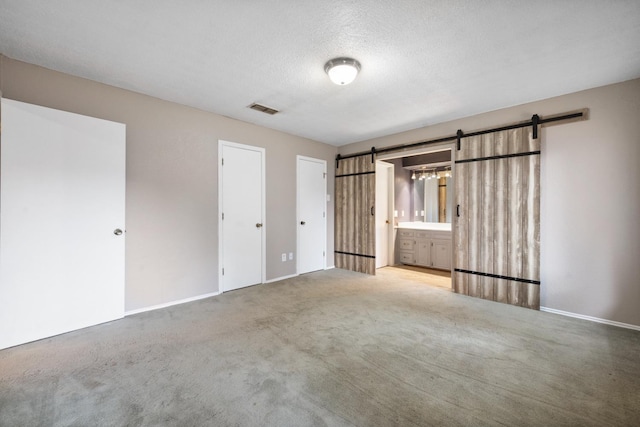 unfurnished bedroom with connected bathroom, a barn door, carpet, and a textured ceiling