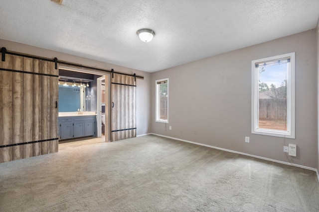 unfurnished room with a barn door, carpet floors, a textured ceiling, and plenty of natural light