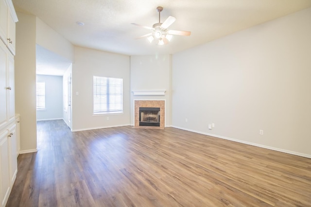 unfurnished living room featuring a tiled fireplace, ceiling fan, and light wood-type flooring