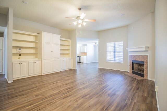 unfurnished living room featuring ceiling fan, dark hardwood / wood-style flooring, and a tile fireplace