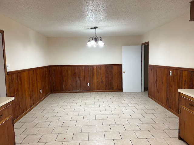 empty room with wooden walls, a textured ceiling, and an inviting chandelier