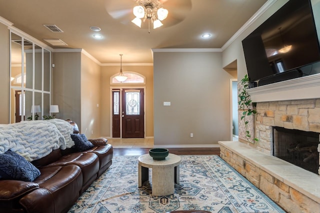 living room with wood-type flooring, a stone fireplace, ornamental molding, and ceiling fan