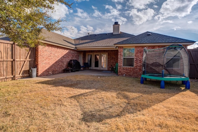 rear view of house with french doors, a lawn, a trampoline, and a patio area