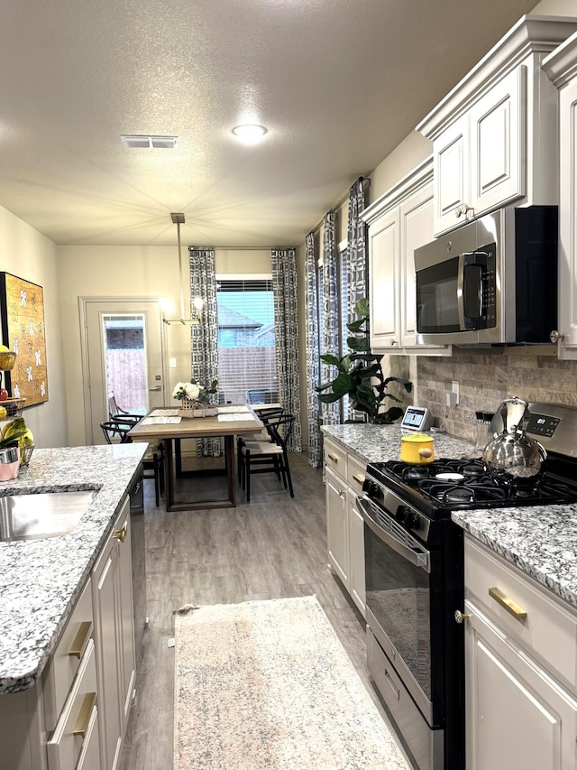 7101 22nd St, Lubbock, TX 79407 - kitchen with black gas range, stainless steel microwave, light wood-style floors, a textured ceiling, and decorative backsplash