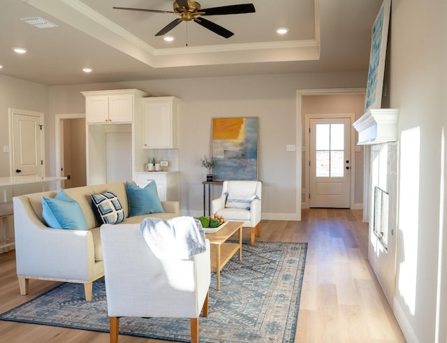 living room with a tray ceiling, ceiling fan, and light wood-type flooring