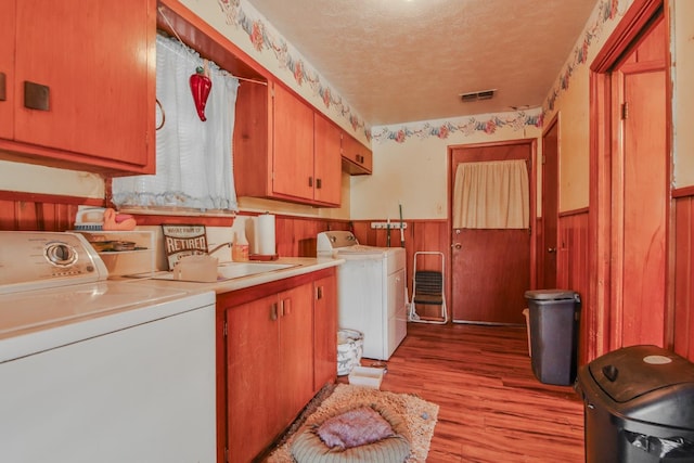 washroom with sink, cabinets, washing machine and dryer, a textured ceiling, and light hardwood / wood-style flooring