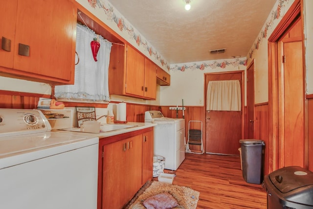 laundry room featuring washing machine and clothes dryer, cabinets, a textured ceiling, wooden walls, and light hardwood / wood-style floors