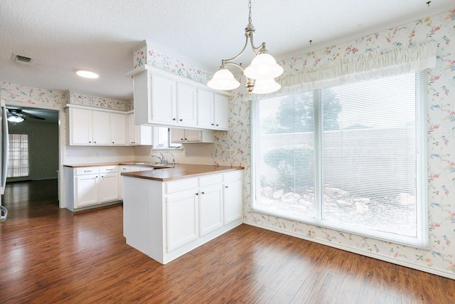 kitchen with dark wood-type flooring, white cabinetry, a textured ceiling, kitchen peninsula, and pendant lighting