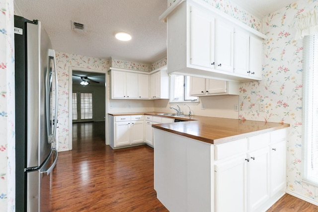 kitchen with white cabinetry, a textured ceiling, stainless steel refrigerator, dark hardwood / wood-style flooring, and kitchen peninsula