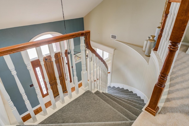 staircase with visible vents, plenty of natural light, a towering ceiling, and carpet floors