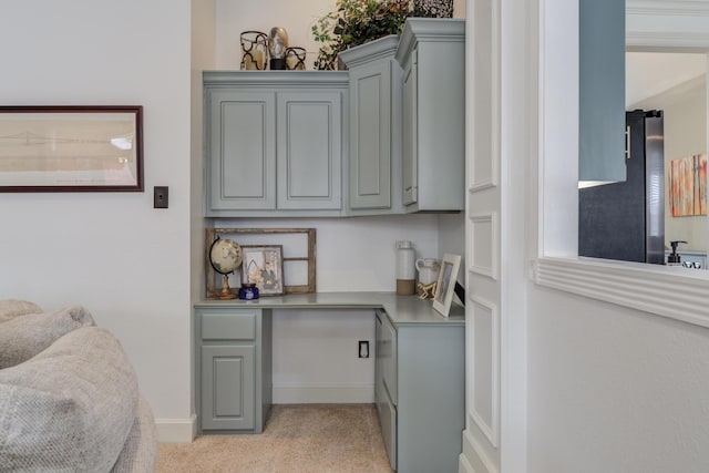 home office featuring built in study area, baseboards, and light carpet