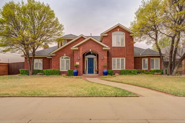 traditional home featuring brick siding, fence, and a front yard