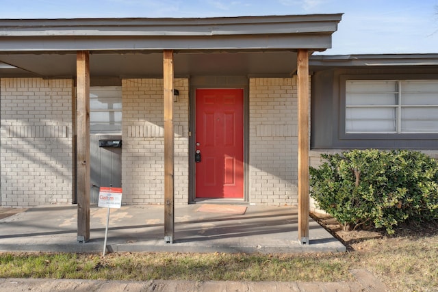 property entrance featuring covered porch and brick siding