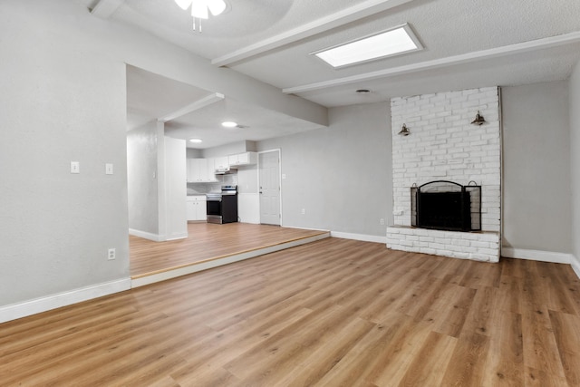 unfurnished living room featuring beam ceiling, baseboards, light wood-style flooring, and a brick fireplace