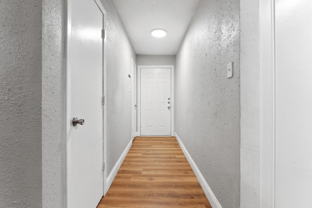 hallway with a textured wall, wood finished floors, and baseboards