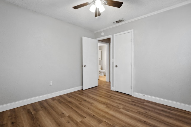 spare room featuring a textured ceiling, visible vents, ceiling fan, baseboards, and wood finished floors