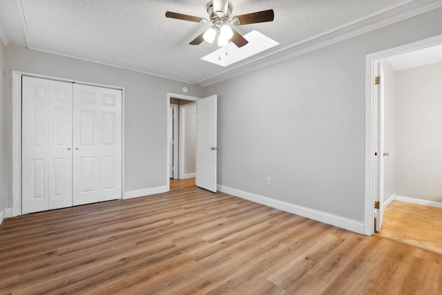 unfurnished bedroom with a skylight, light wood-style flooring, a closet, baseboards, and a textured ceiling