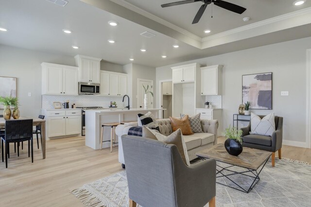 living room featuring ornamental molding, a tray ceiling, sink, and light hardwood / wood-style flooring