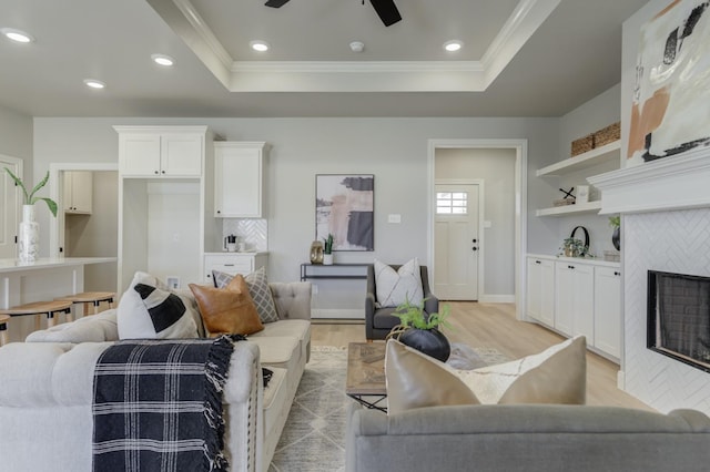 living room featuring crown molding, a raised ceiling, light hardwood / wood-style floors, and a tile fireplace