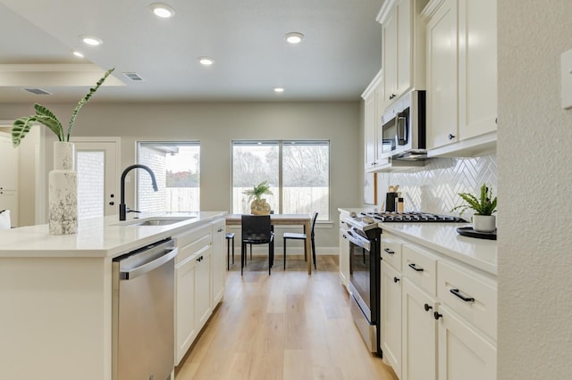 kitchen with stainless steel appliances, a kitchen island with sink, sink, and white cabinets