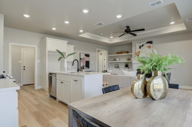 kitchen featuring dishwasher, white cabinets, a kitchen island with sink, a tray ceiling, and light hardwood / wood-style flooring