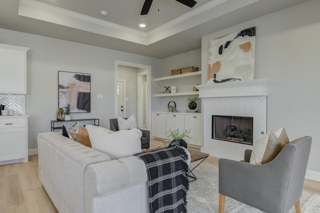 living room with ornamental molding, light hardwood / wood-style flooring, a fireplace, and a tray ceiling