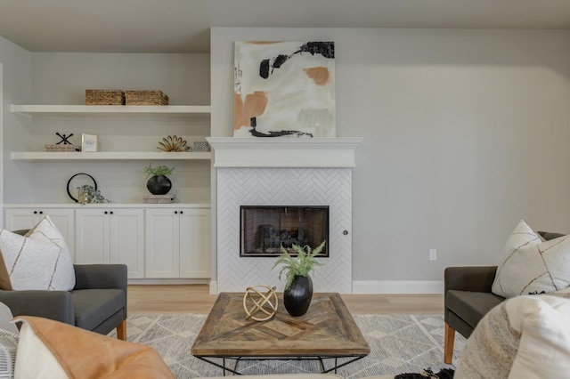 living room with a tiled fireplace, built in features, and light wood-type flooring